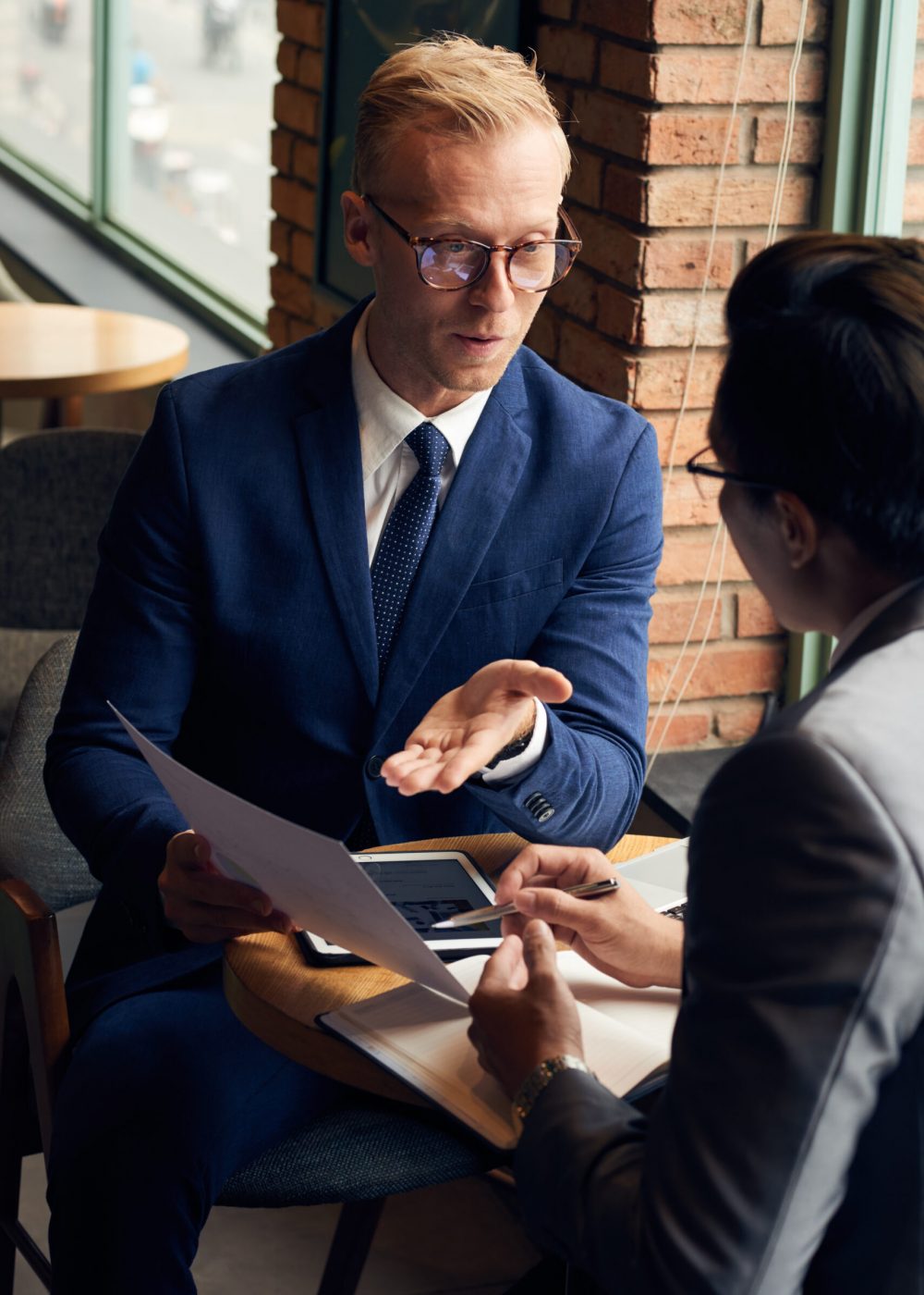 Young businessman in glasses showing contract to partner during a strategy meeting in a cafe